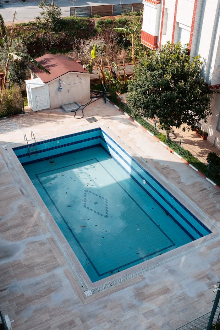 An empty swimming pool in a sunlit garden in Antalya, Türkiye, surrounded by lush greenery.